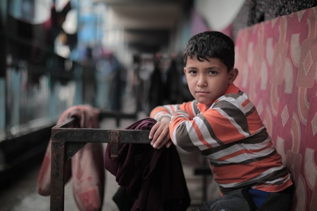 The boy above sits clutching a ragged blanket in an UNRWA school-turned-refugee center